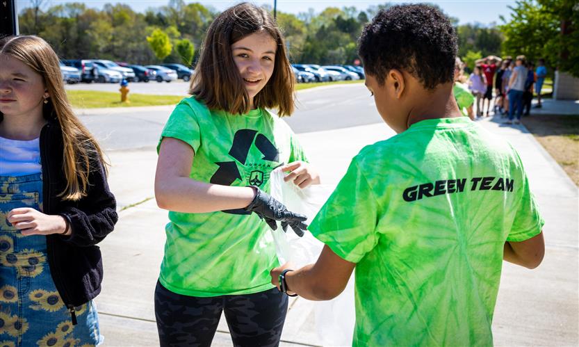 Two students wearing Green Team t-shirts pick up trash